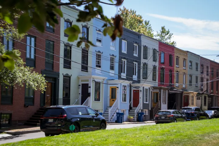 Row of colorful houses on a street with parked cars and trees.