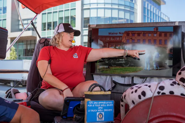 Tour guide in red shirt pointing at a screen during an outdoor presentation.