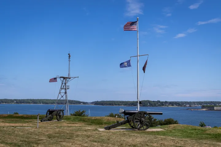 Cannons and flags by a river with a clear blue sky.